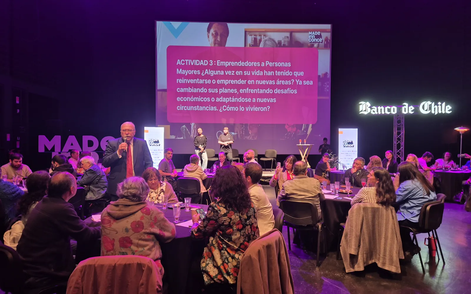 Un participante comparte su experiencia con el micrófono durante la actividad sobre reinventarse, con la sala llena de mesas, en MadeInnConce 2025